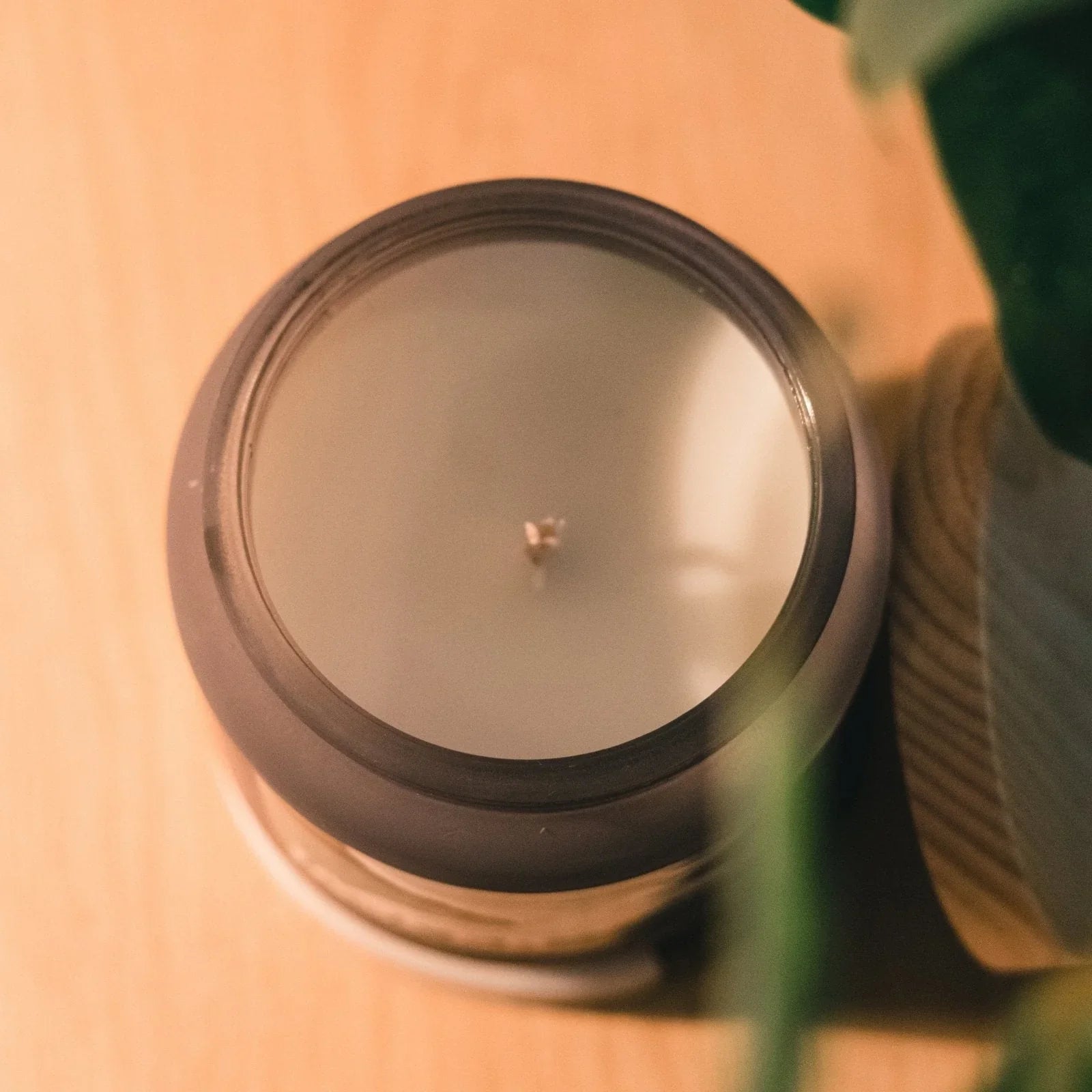 Dark amber peony scented candle in a glass jar on a wooden surface