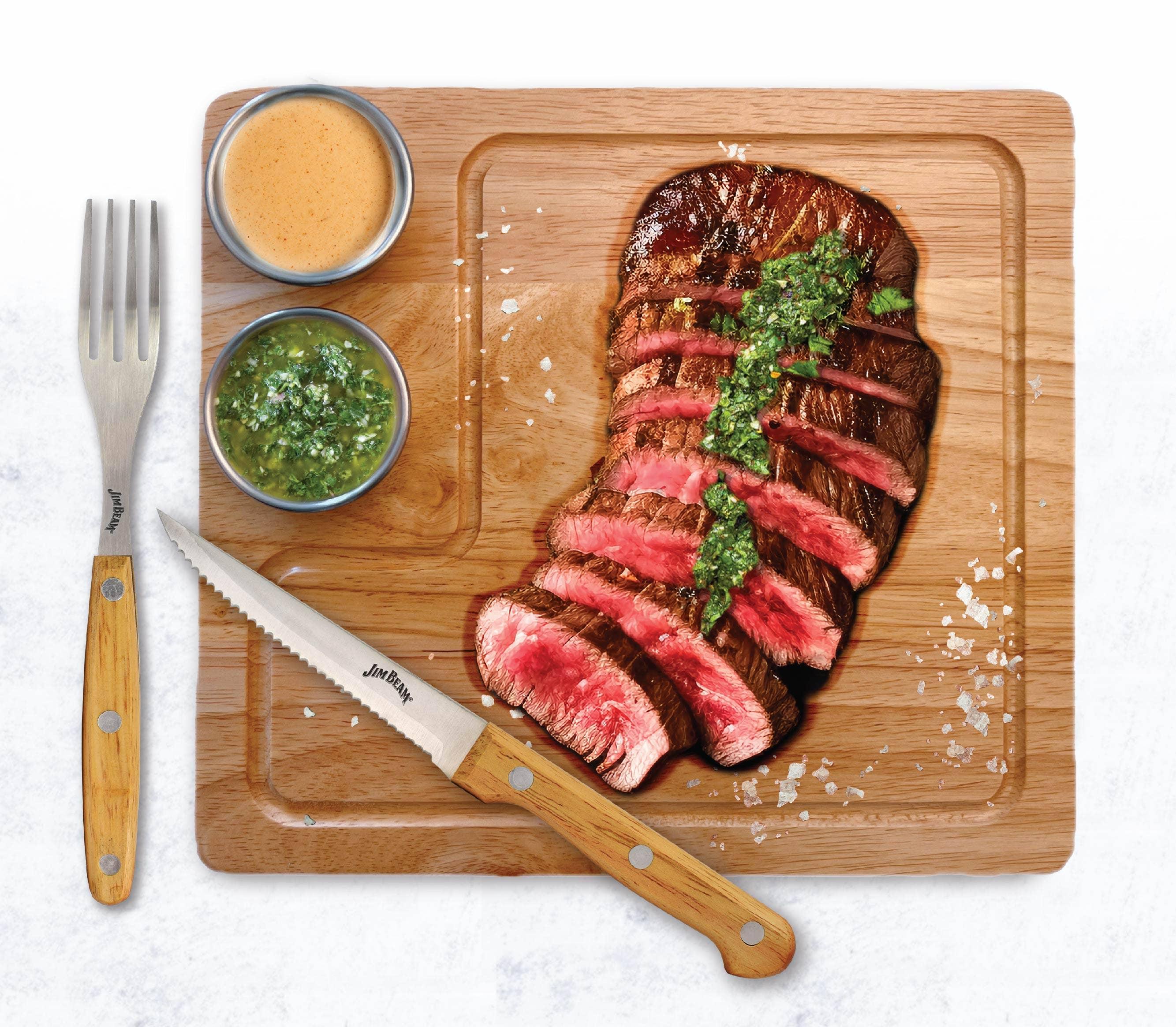 Sliced grilled steak with chimichurri on wooden board, steak knife, dipping sauces, coarse salt