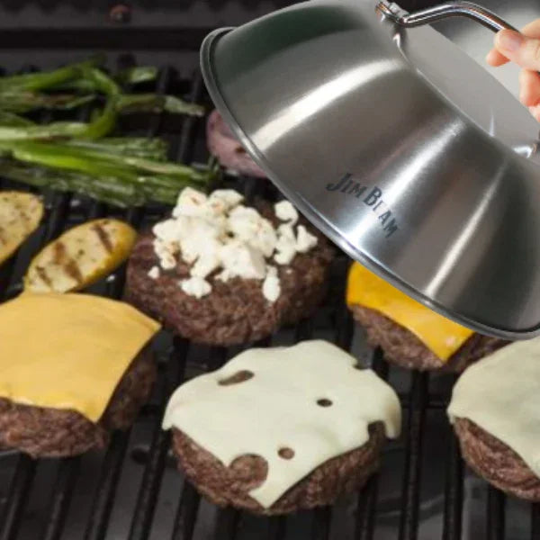 Grill with burgers topped with cheese, veggies, and a stainless steel Jim Beam melting dome