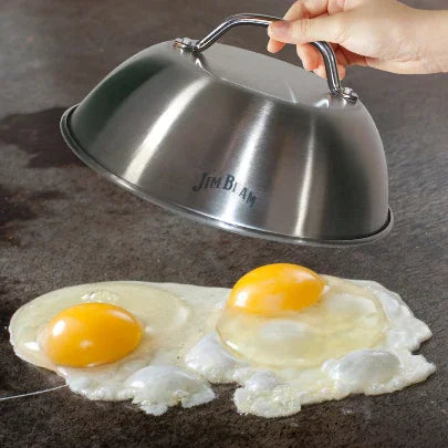 Hand lifting stainless steel Jim Beam grill dome over two frying eggs on flat top griddle
