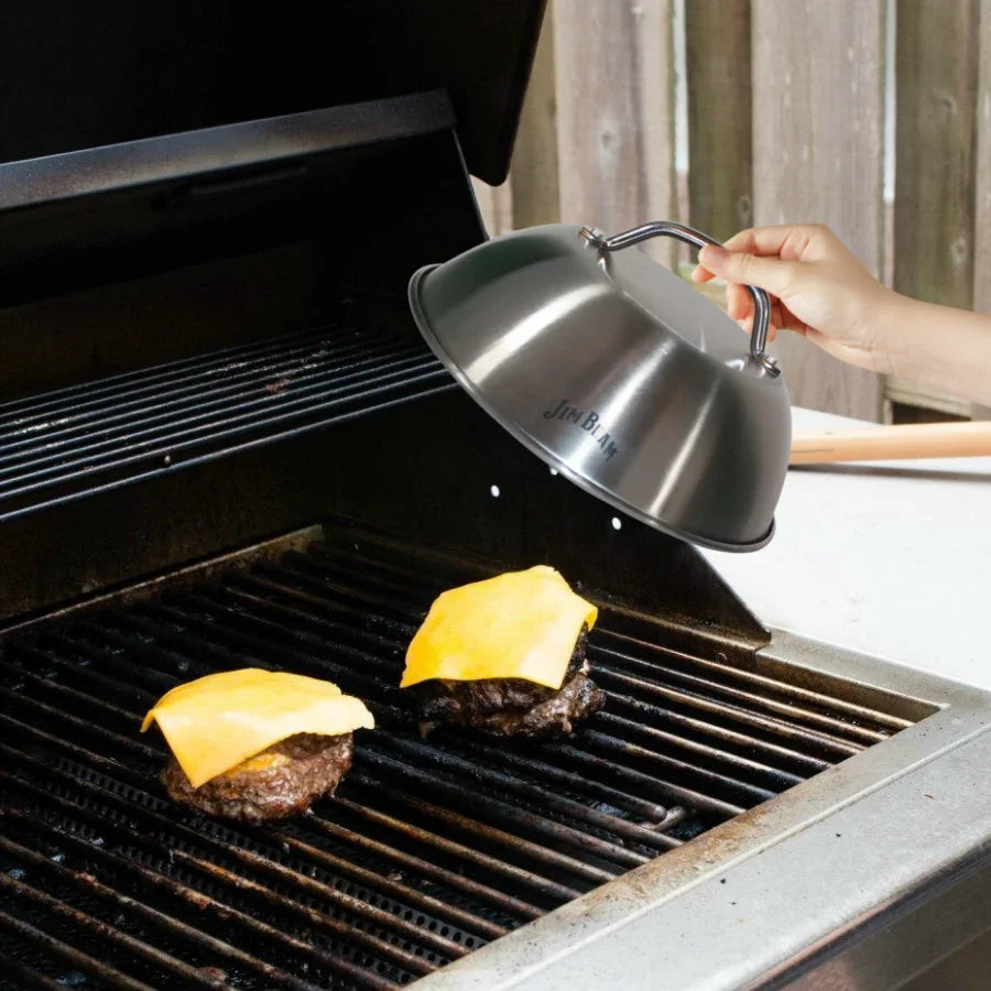 Hand using stainless steel melting dome on grill with burgers and melted cheese