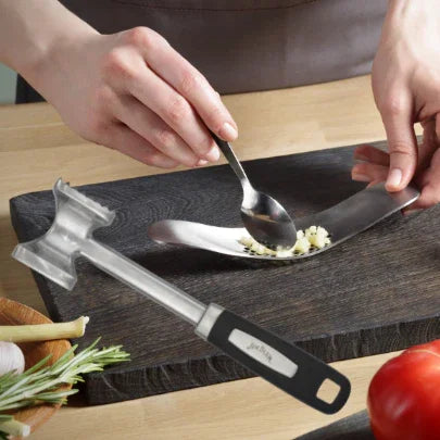 Person using a garlic crusher tool on a cutting board in a kitchen with fresh vegetables