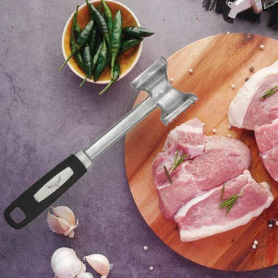 Meat tenderizer on wooden board with raw pork chops, garlic, green chili peppers