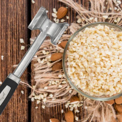 Chopped almonds in glass bowl with meat tenderizer on rustic wooden table