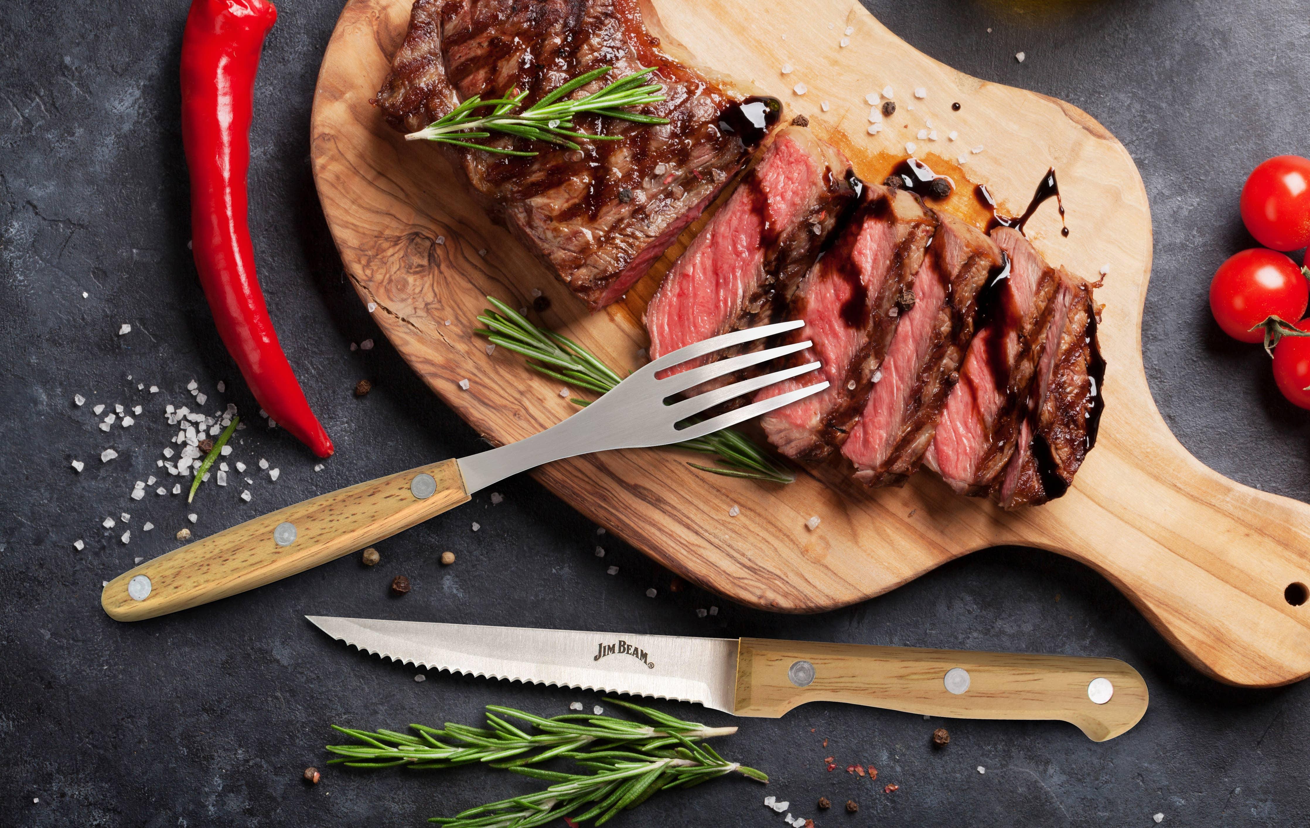 Sliced grilled steak with rosemary and balsamic glaze on wooden board, chili, tomatoes, cutlery