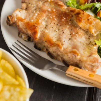 Grilled pork ribs on a plate with salad and chips, barbecue dinner food