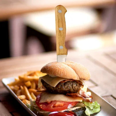 Cheeseburger with lettuce, tomato, bacon, and knife in bun, served with fries on a plate