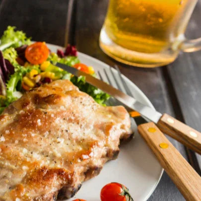 Grilled pork chop with fresh salad and cherry tomatoes on plate, beer mug in background