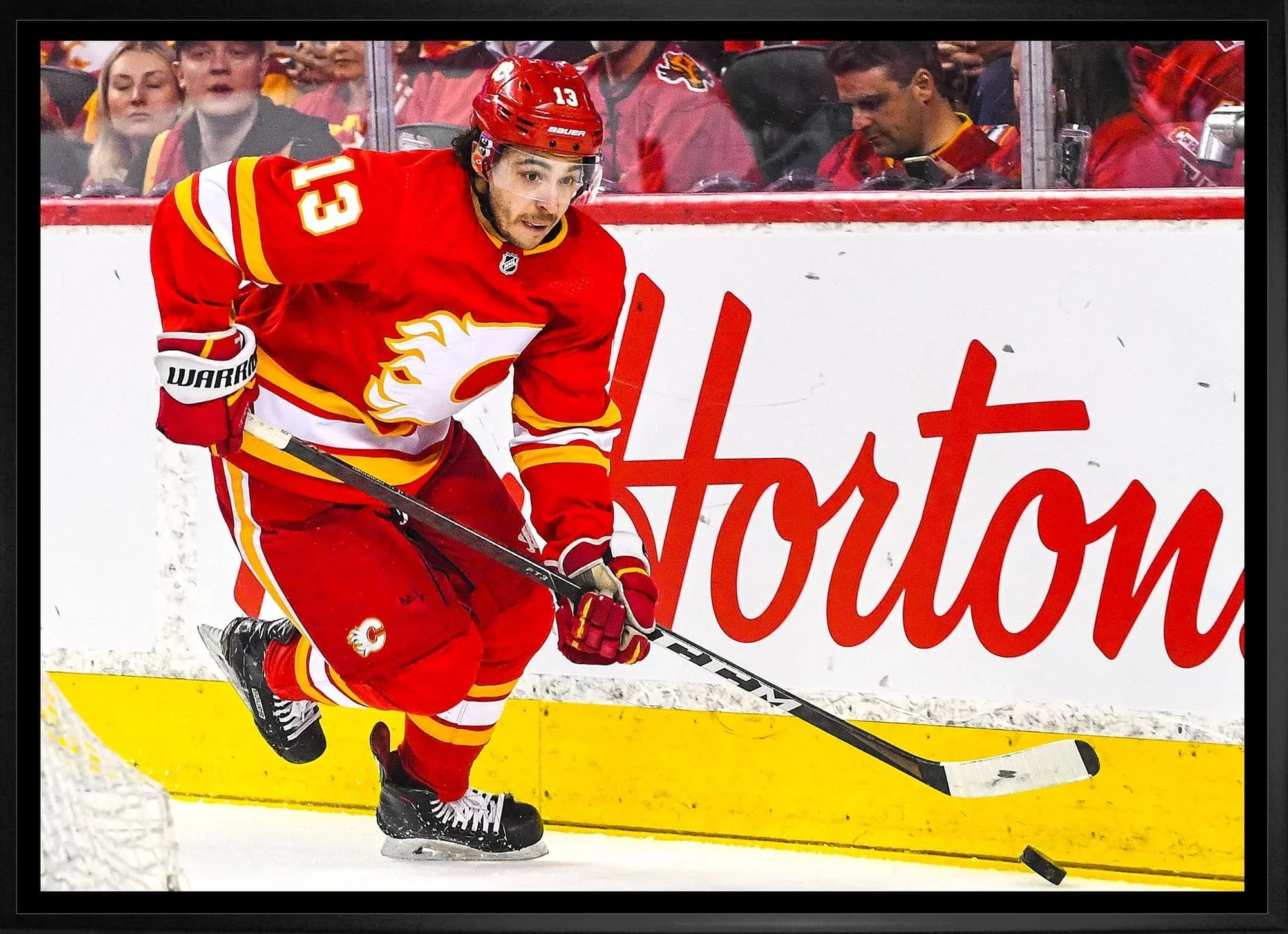 Calgary Flames hockey player in red uniform skating during game, Tim Hortons ad in background