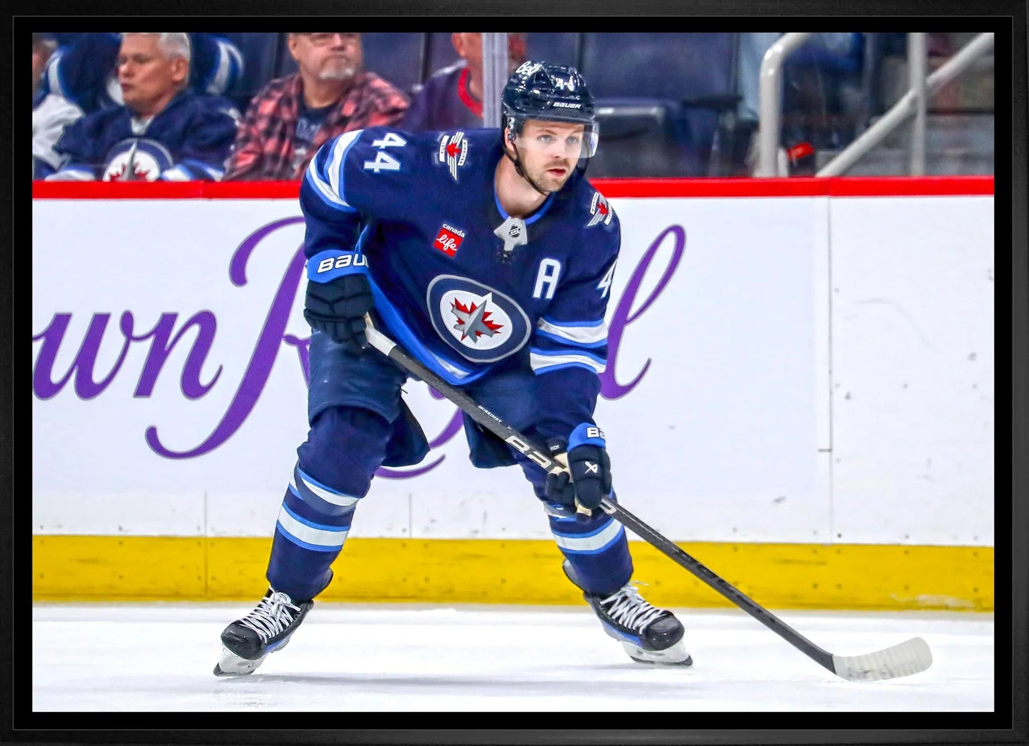 Winnipeg Jets hockey player in blue uniform skating on ice during game, fans in background