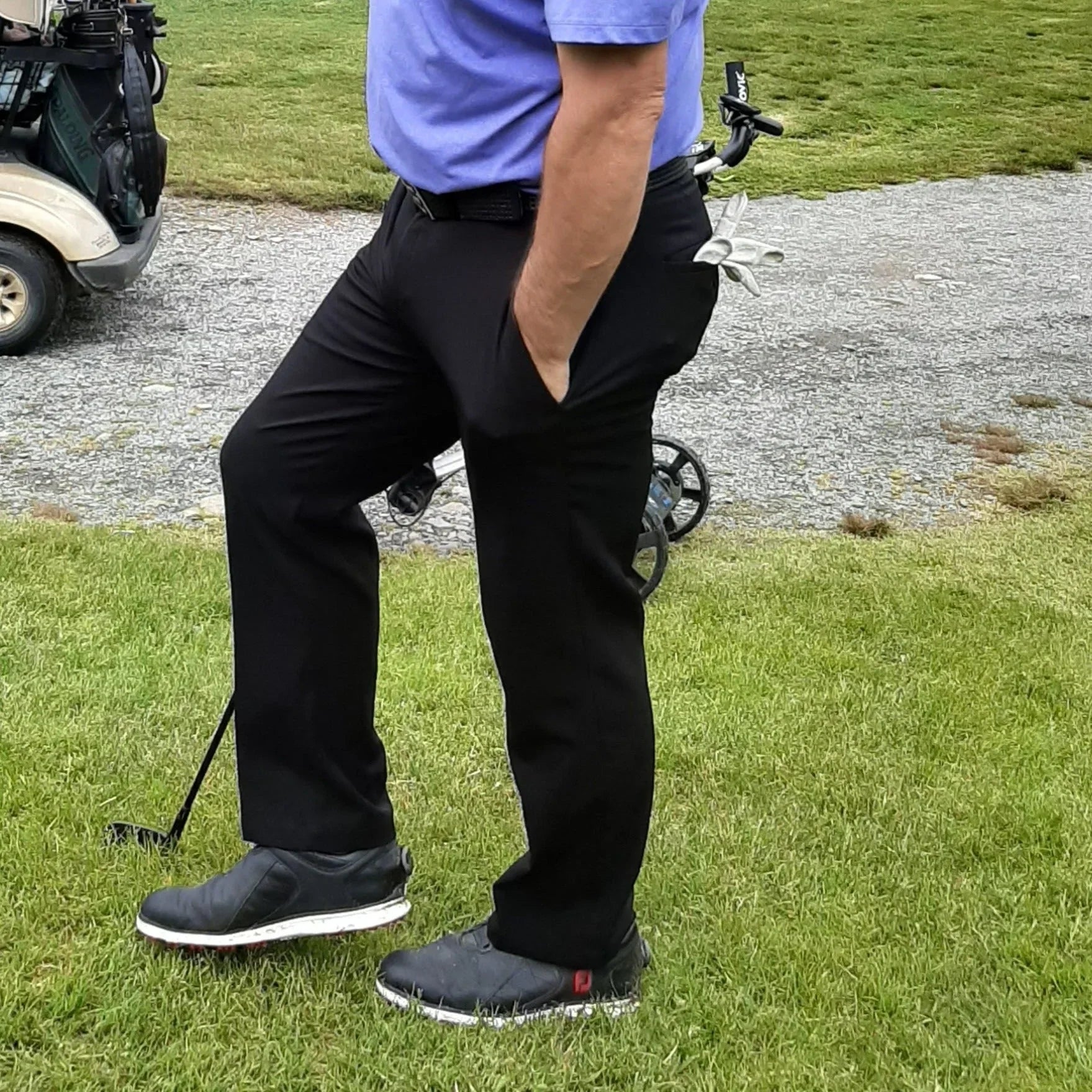 Man in black golf pants and black slip-on golf shoes on golf course near cart and clubs