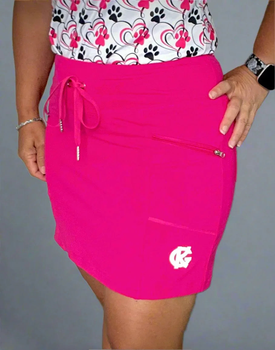 Woman wearing bright pink golf skort with drawstring, pocket, and logo, sporty style
