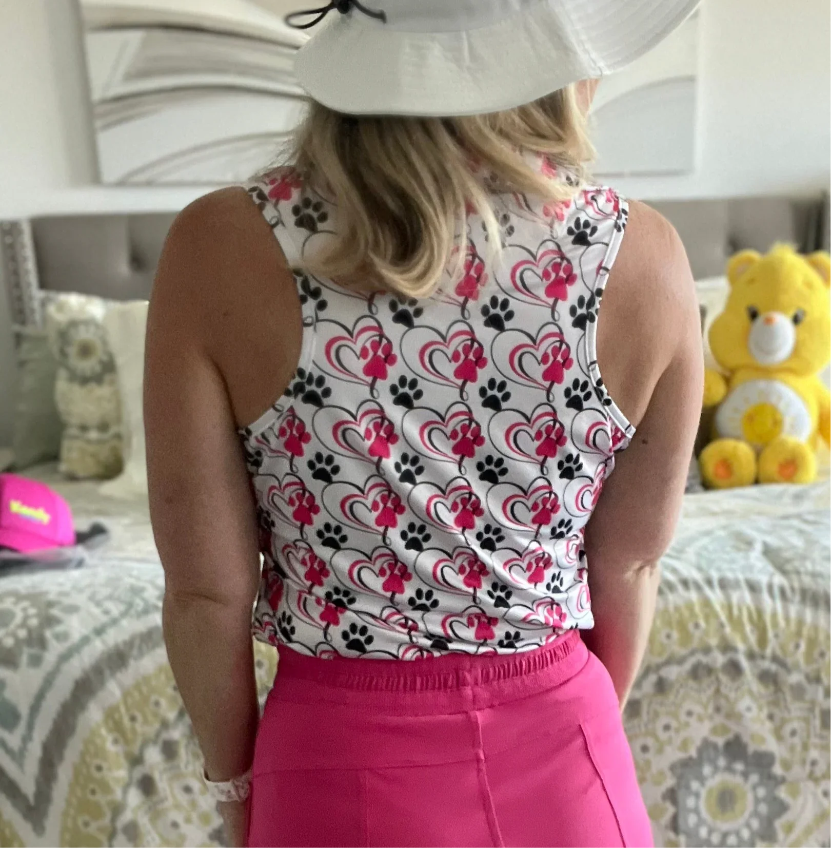 Woman in a white hat and heart paw print top with pink skirt, standing in bedroom