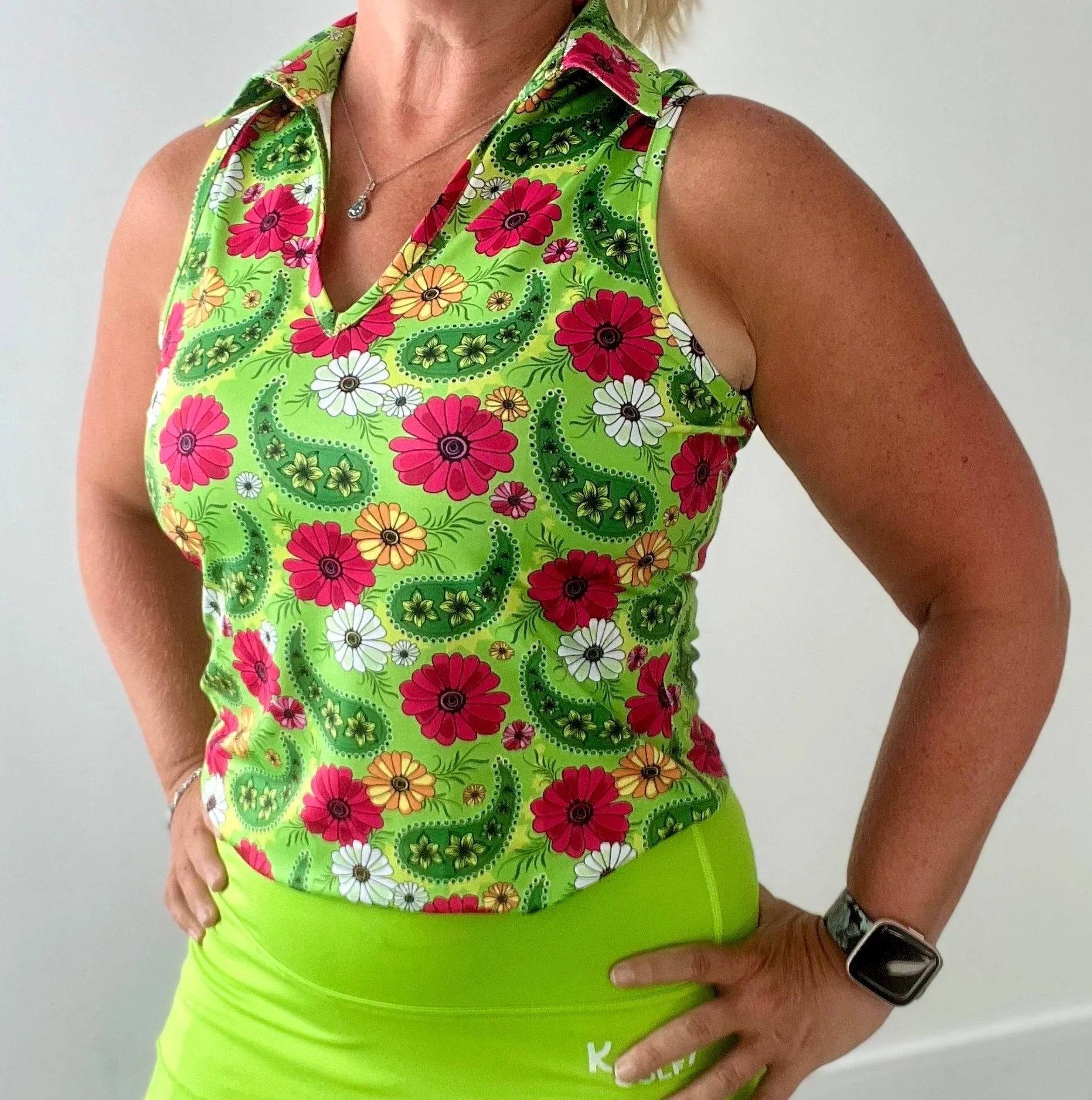 Woman wearing sleeveless green floral polo shirt and neon green skirt, standing indoors