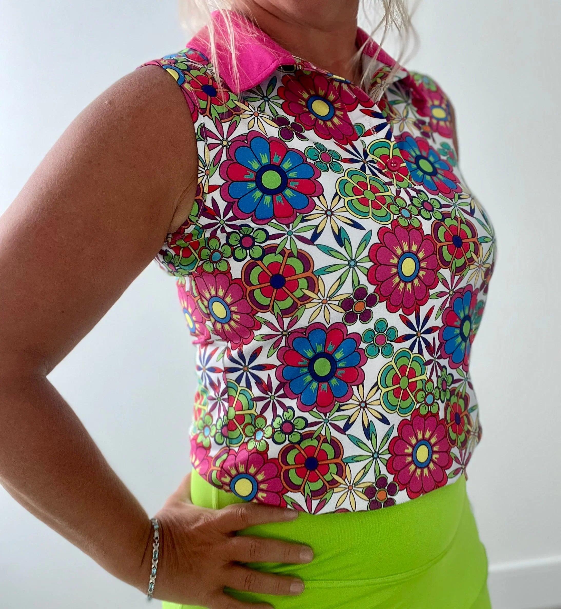 Woman wearing sleeveless floral print polo shirt with neon green skirt against white wall