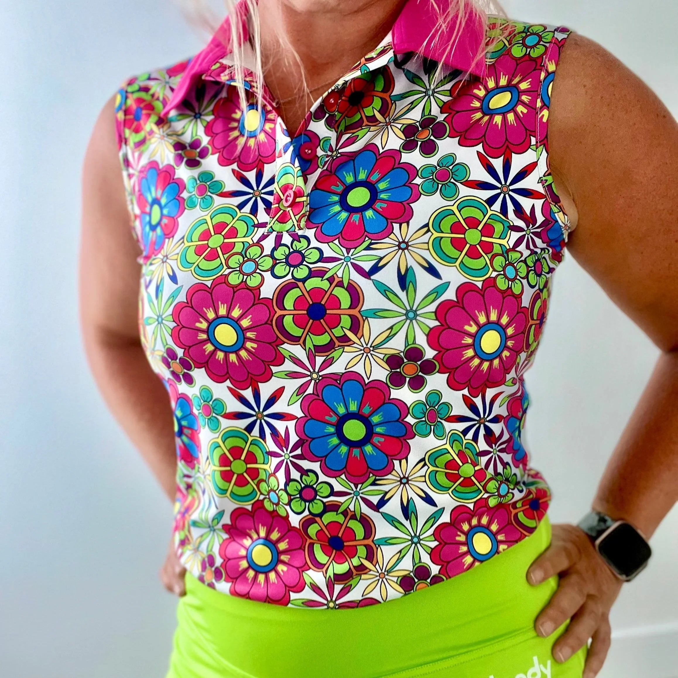Woman in sleeveless floral print golf shirt and neon green skirt standing indoors