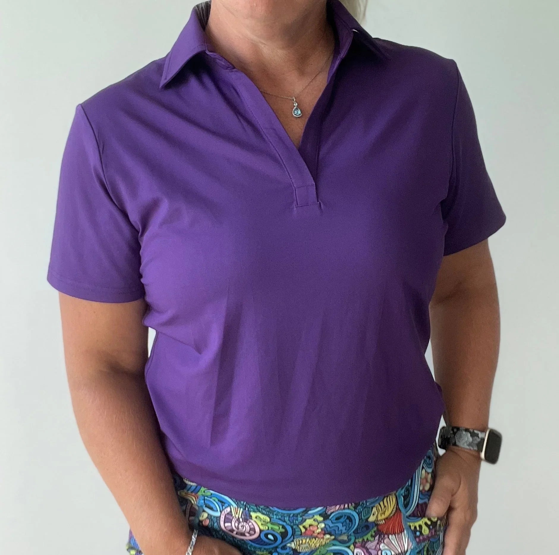 Woman wearing a purple short sleeve golf polo shirt and colorful printed skirt