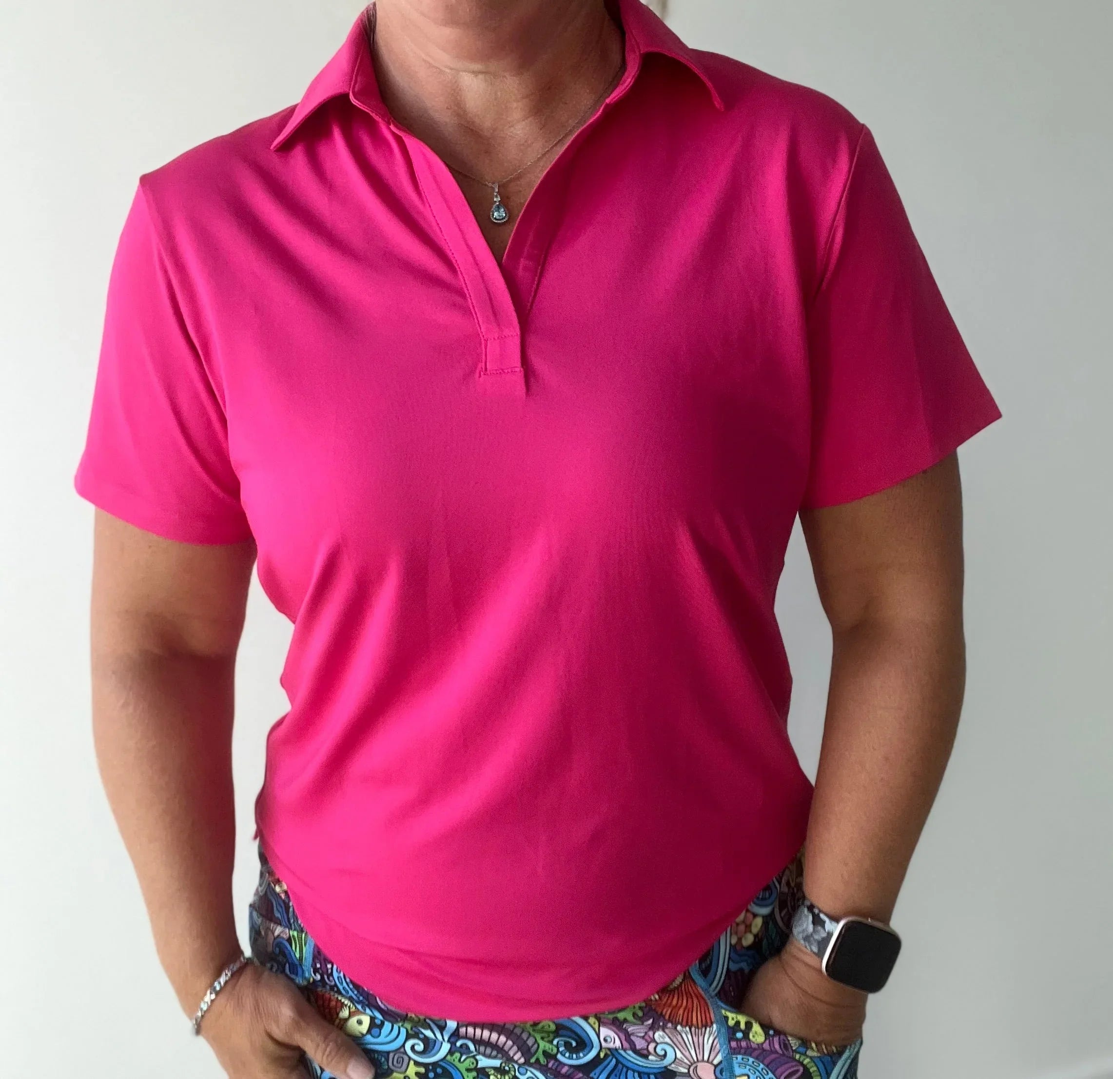 Woman wearing a bright pink short sleeve golf polo and colorful patterned skirt