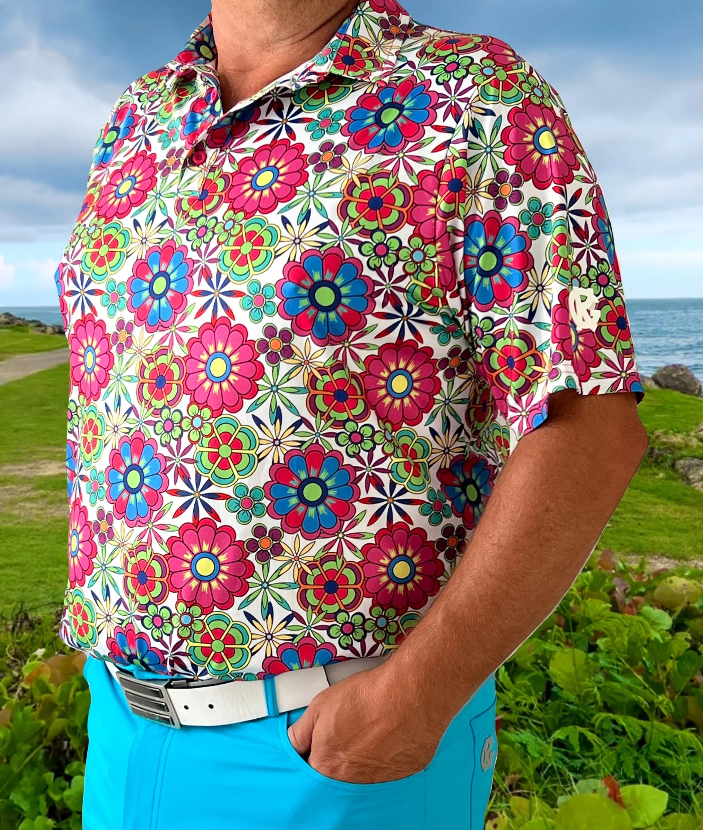 Man wearing a colorful floral golf shirt and blue pants outdoors near the coast