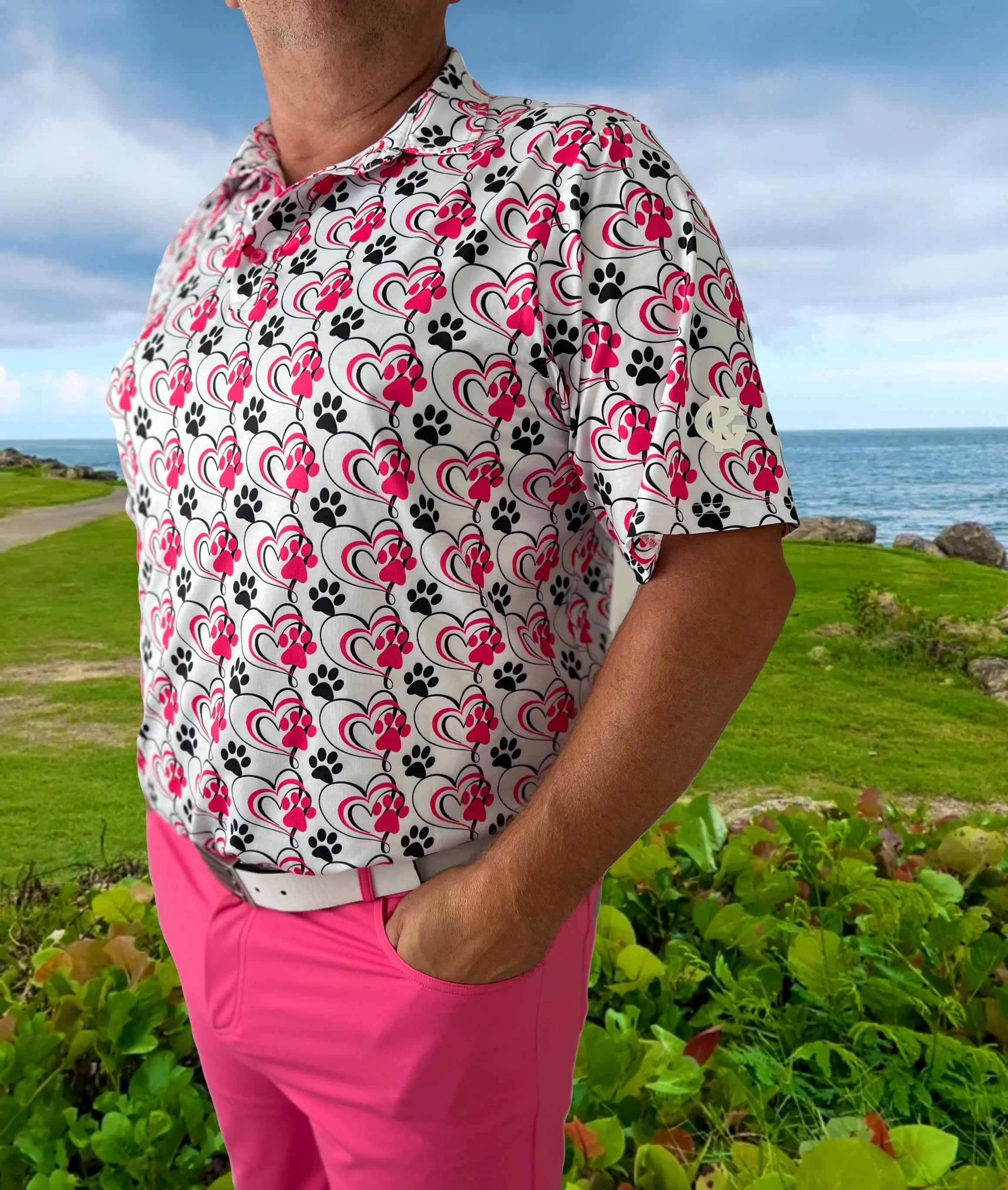 Man wearing pink paw print heart polo shirt and pink pants outdoors by the ocean