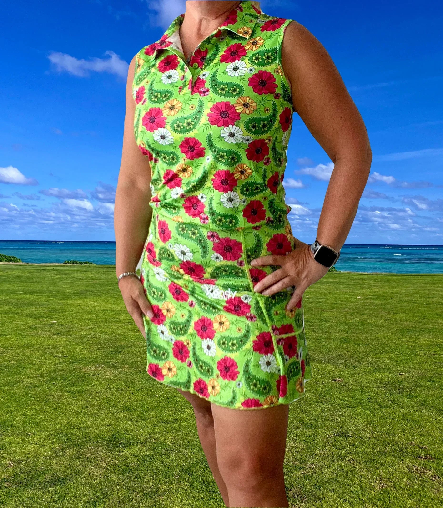 Woman in sleeveless floral golf dress standing on golf course by ocean and blue sky