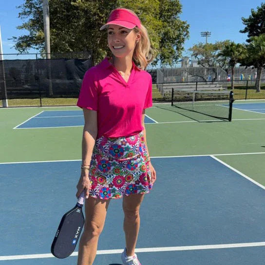 Woman in pink shirt and visor with pickleball paddle on outdoor court