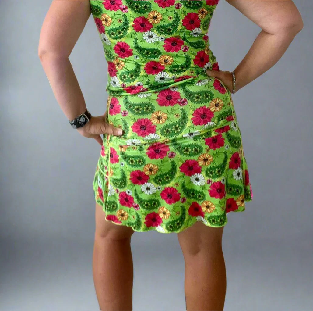 Woman in green floral print dress posing with hands on hips, gray background