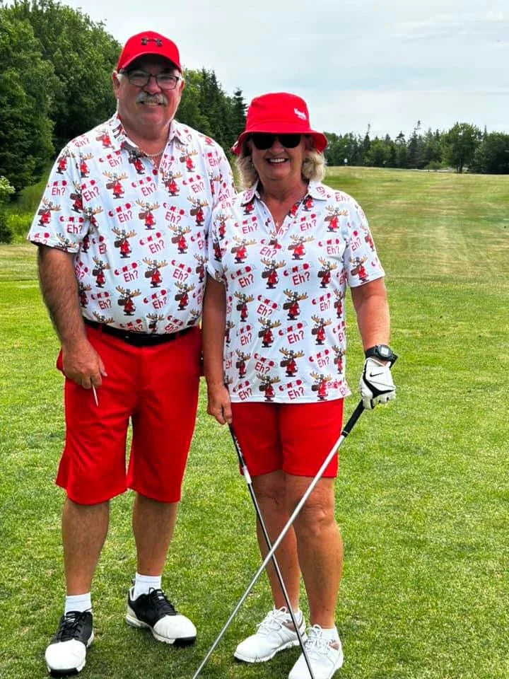Two golfers in matching red shorts and Canadian-themed shirts on a green golf course.