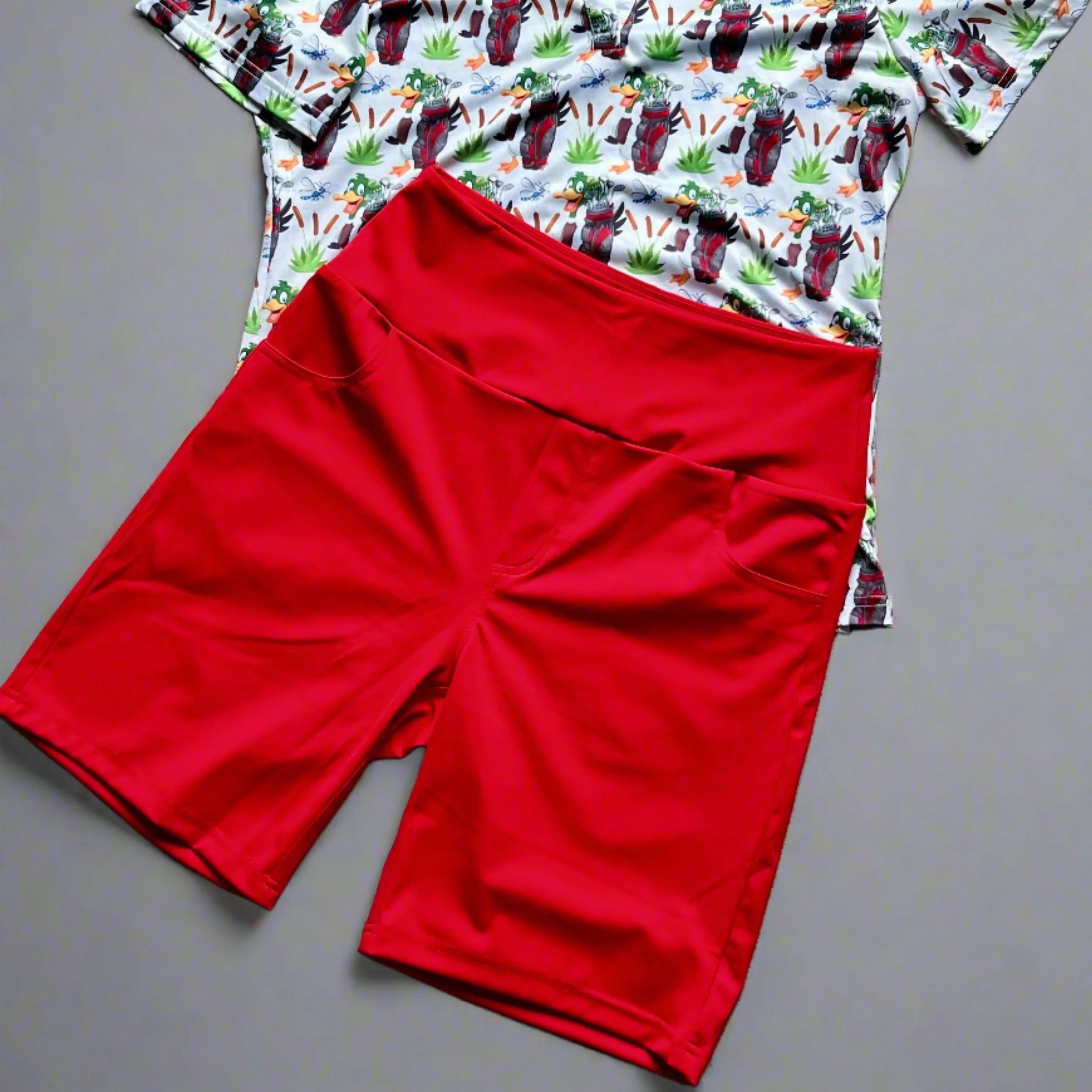 Red athletic shorts with pockets on top of a printed t-shirt, flat lay on grey background