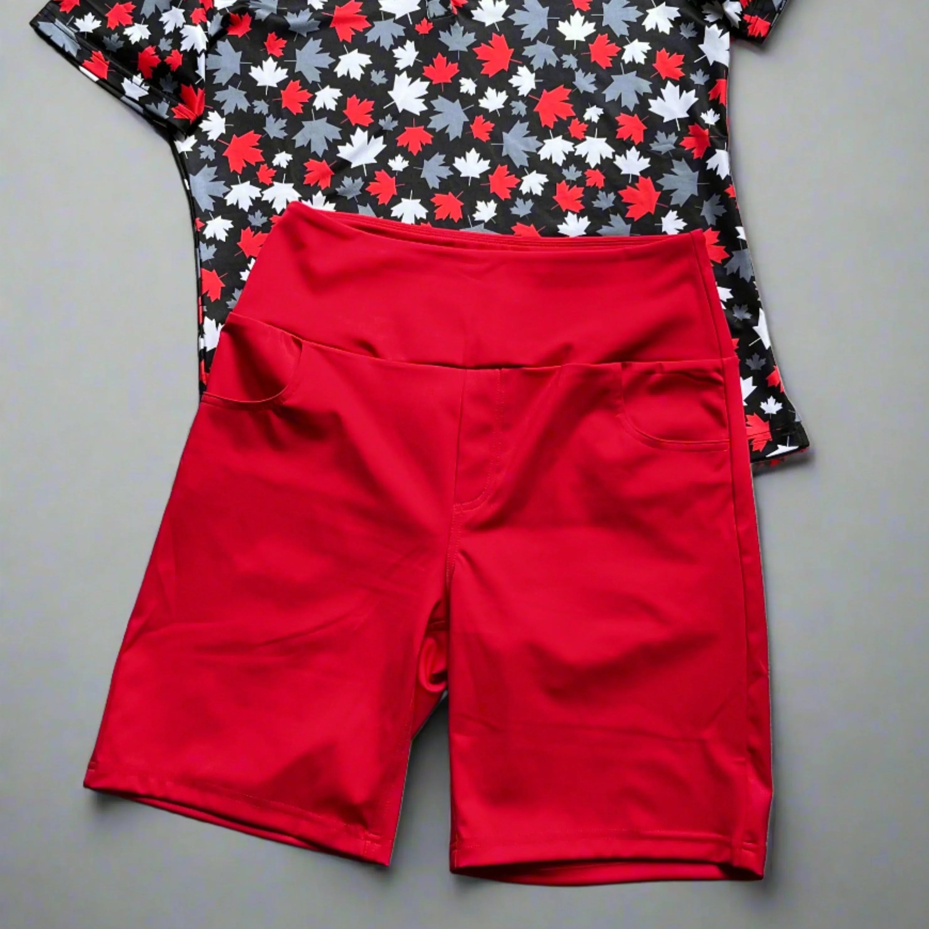 Red athletic shorts with pockets paired with maple leaf print black t-shirt on grey background