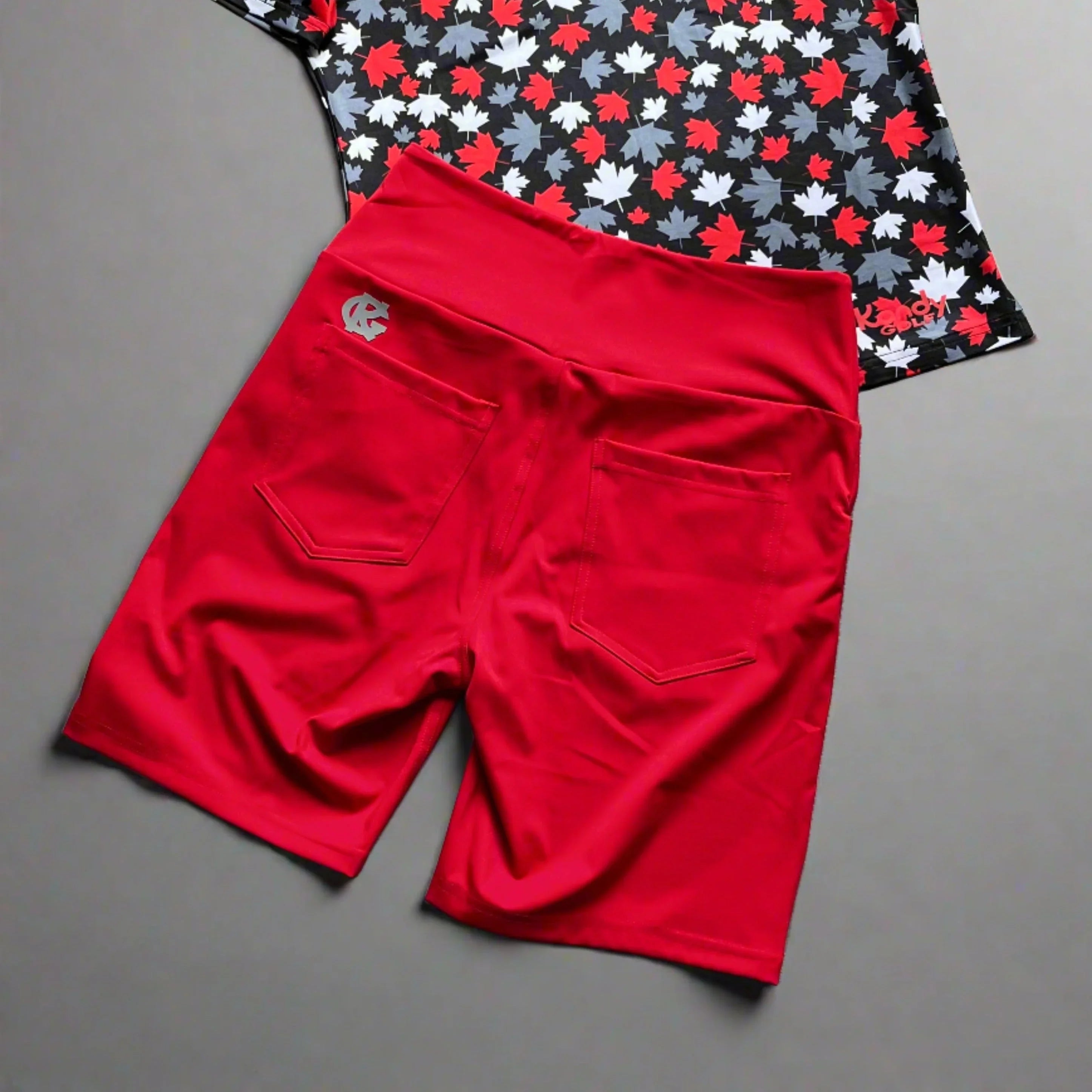 Red athletic shorts with pockets and maple leaf print shirt on gray background