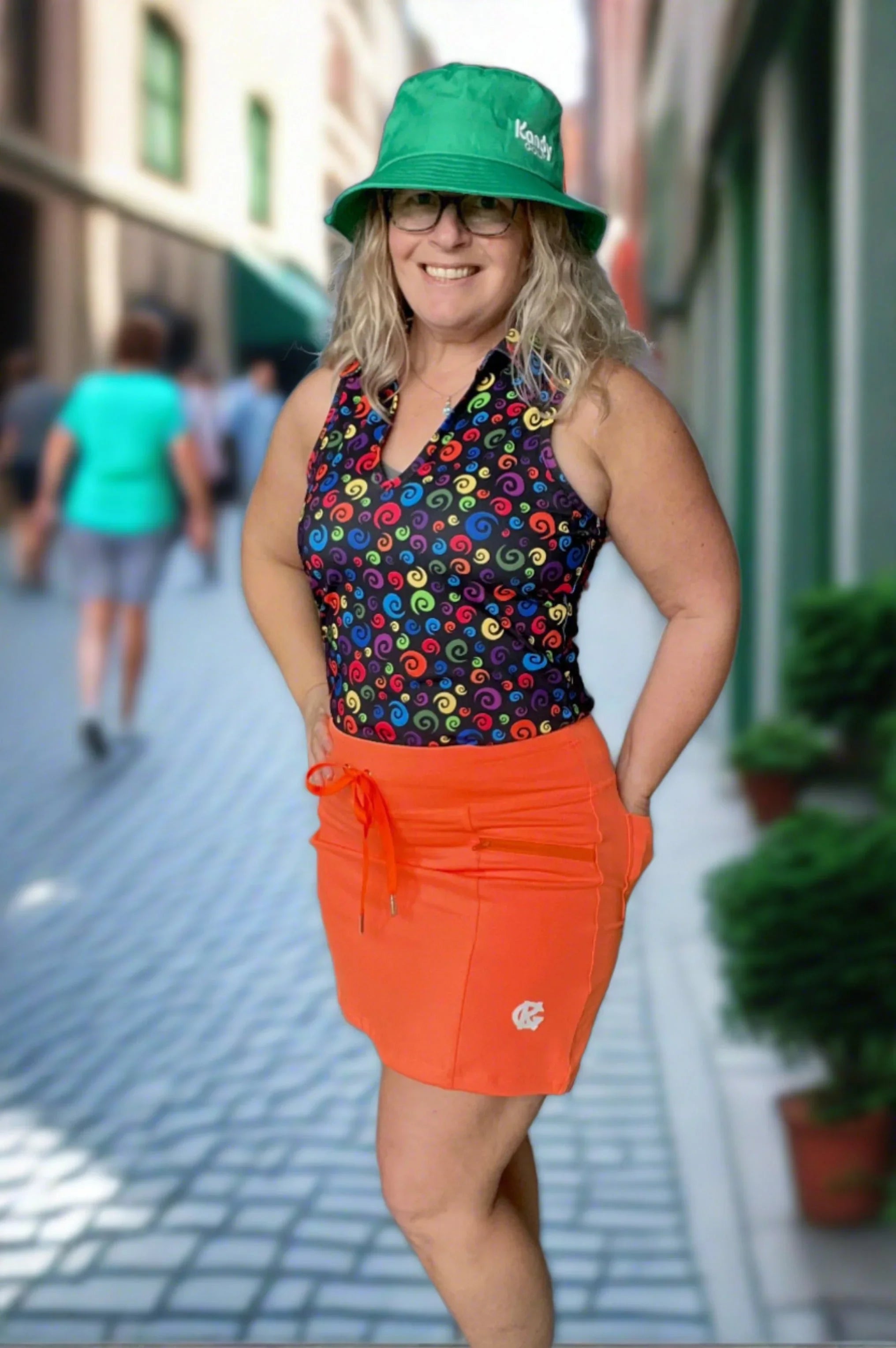 Smiling woman in green bucket hat, colorful swirl tank top, orange skirt on city street