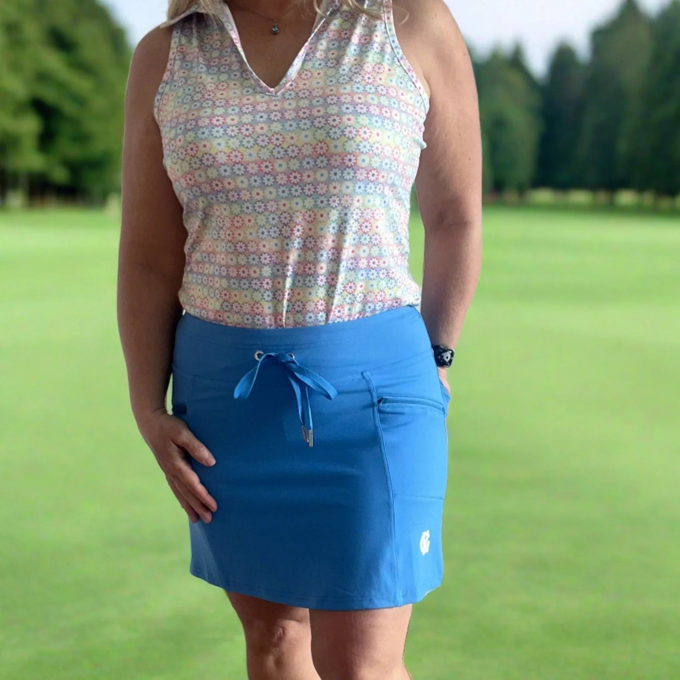 Woman wearing sleeveless floral golf top and blue sport skirt on green golf course