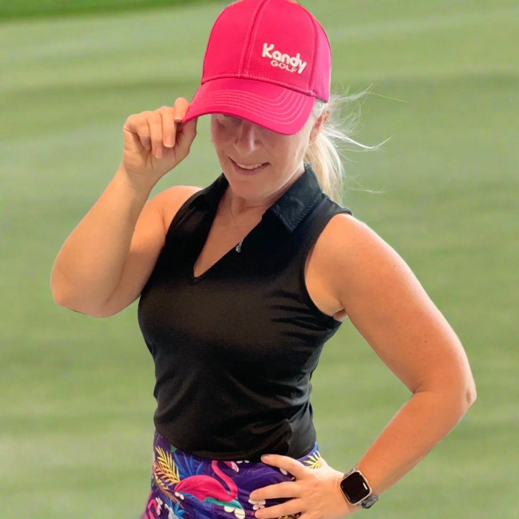 Woman in pink Kandy Golf hat and golf attire posing on golf course