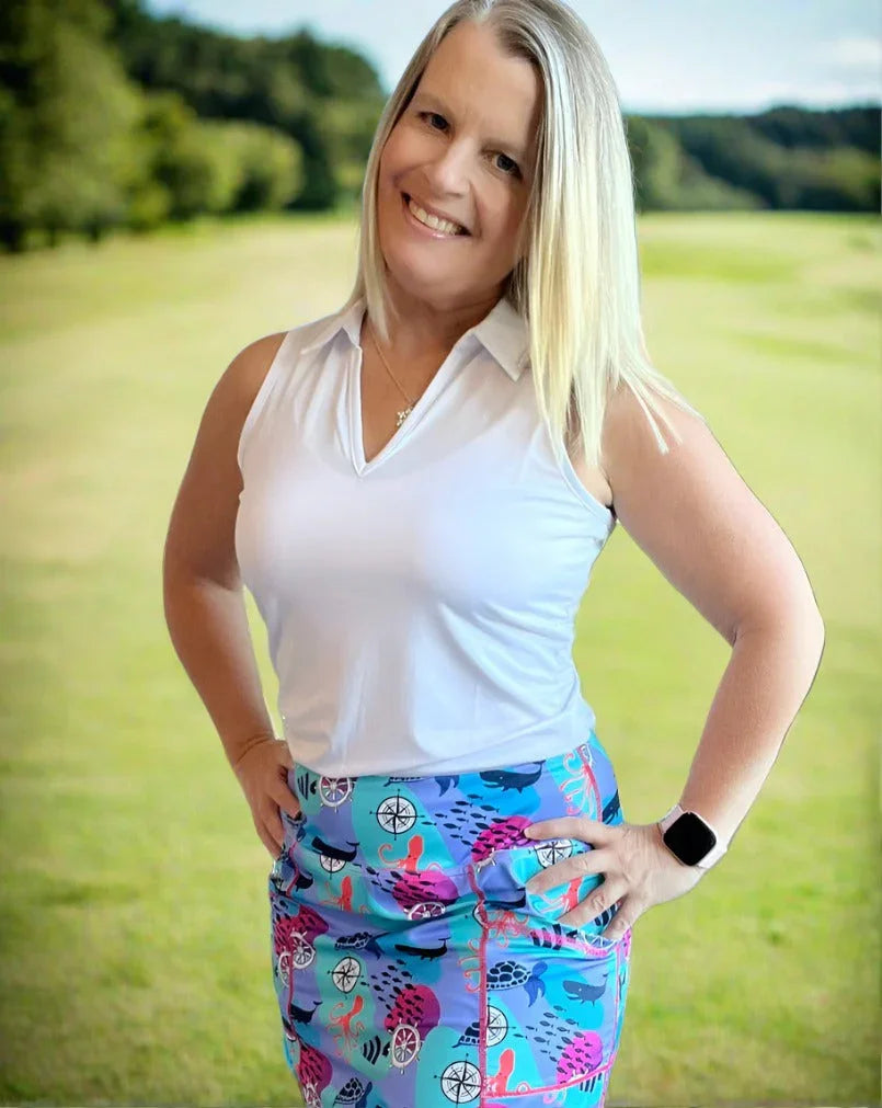 Woman in sleeveless white golf shirt and colorful skirt smiling on a golf course