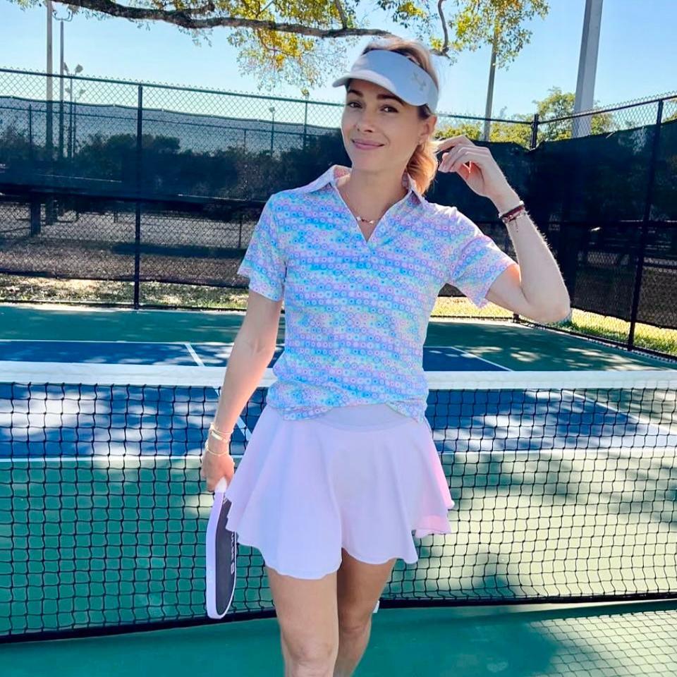 Woman in pastel tennis outfit holding pickleball paddle on outdoor court