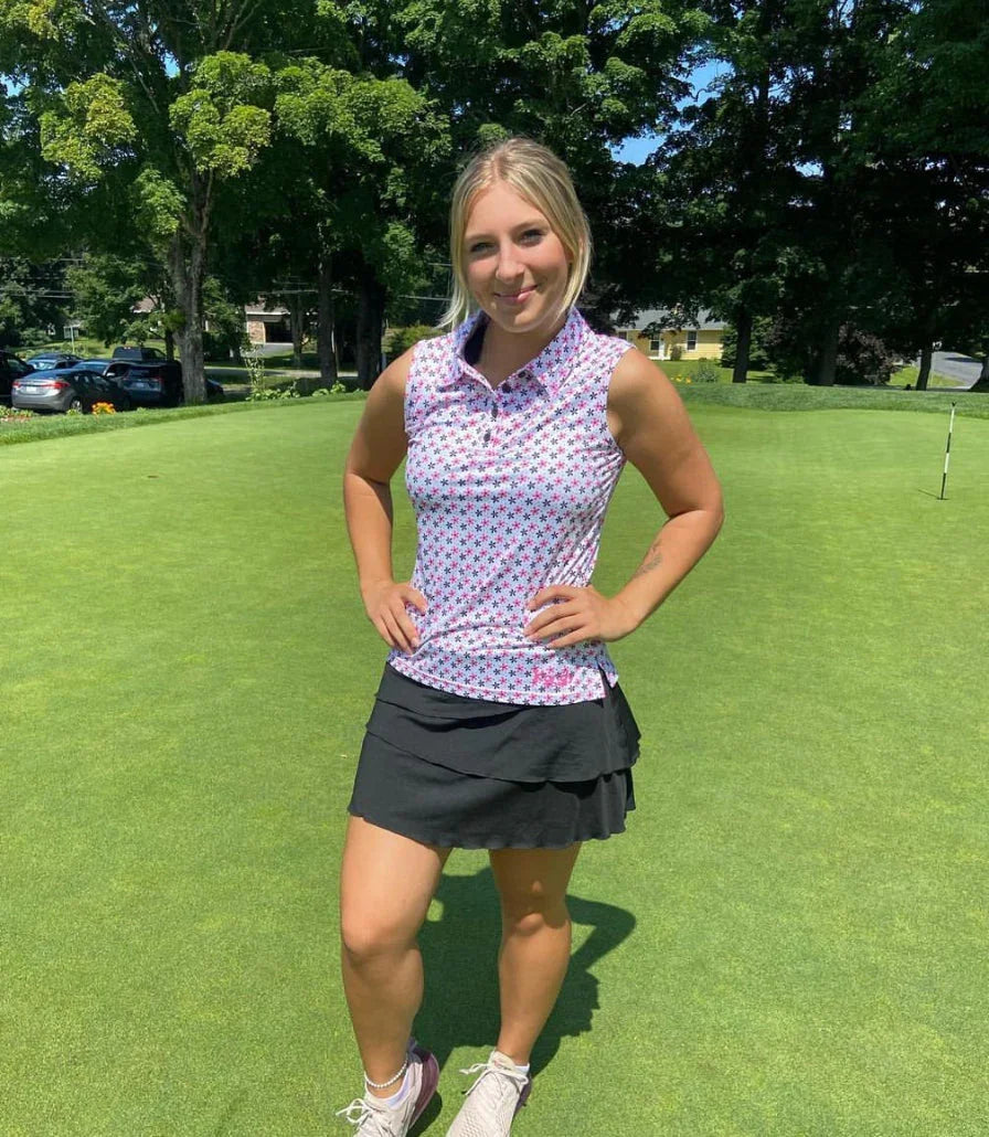 Woman in golf attire standing on green golf course with trees and sunny weather