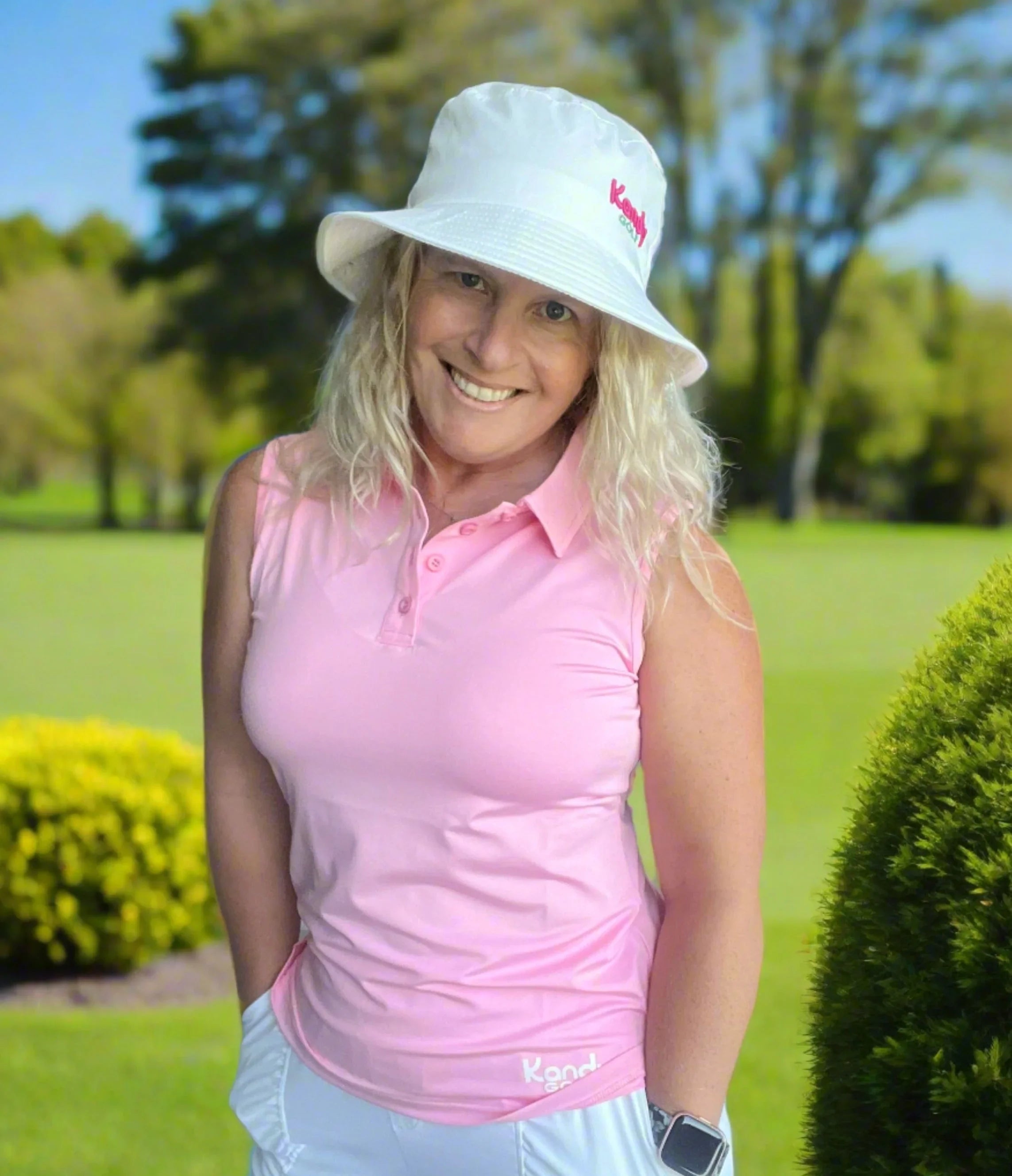 Woman in pink golf shirt and white bucket hat smiling on a sunny golf course