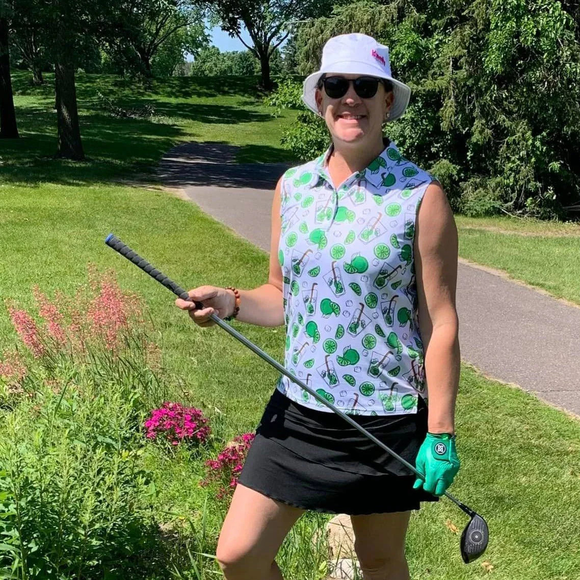 Woman golfer in sleeveless patterned shirt, white bucket hat, and sunglasses on sunny golf course