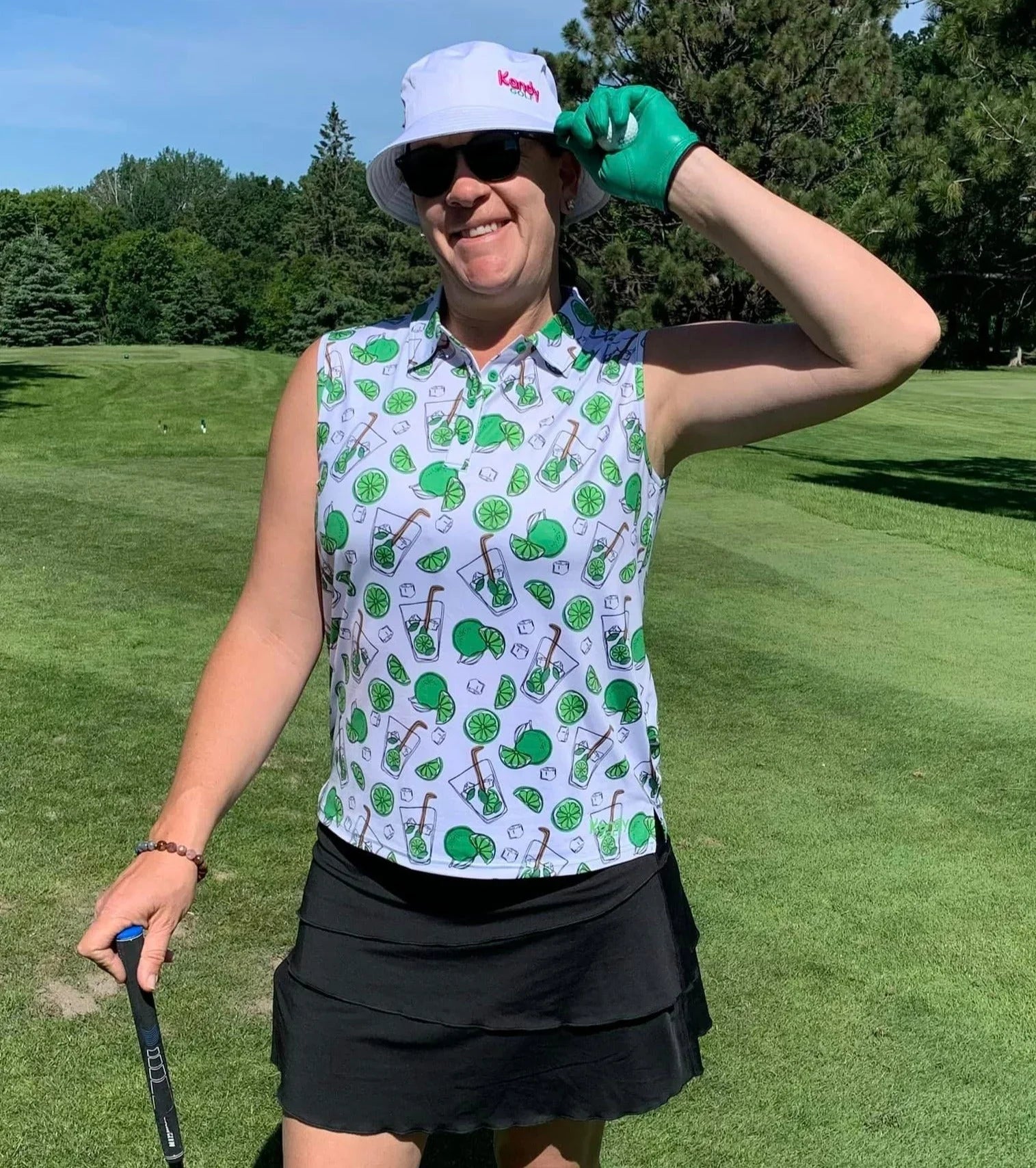 Smiling woman golfer in bucket hat, sunglasses, and printed sleeveless polo on green golf course