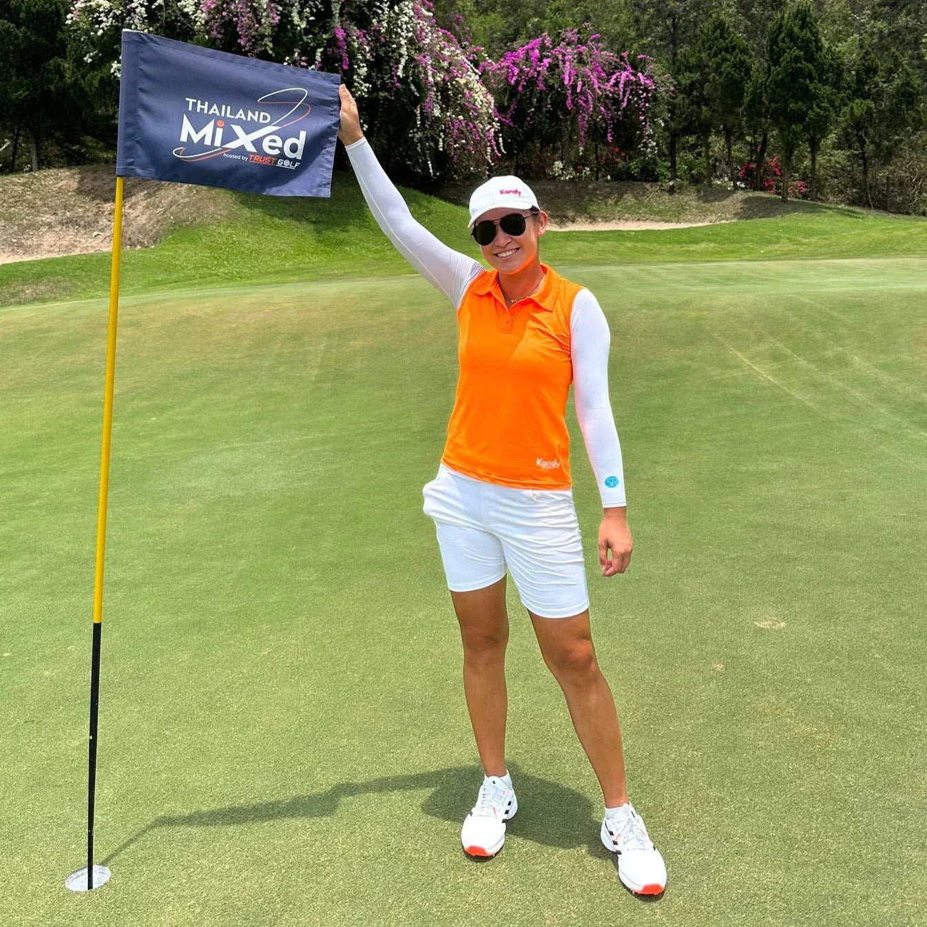 Female golfer poses with Thailand Mixed flag on golf green in sunny outdoor course