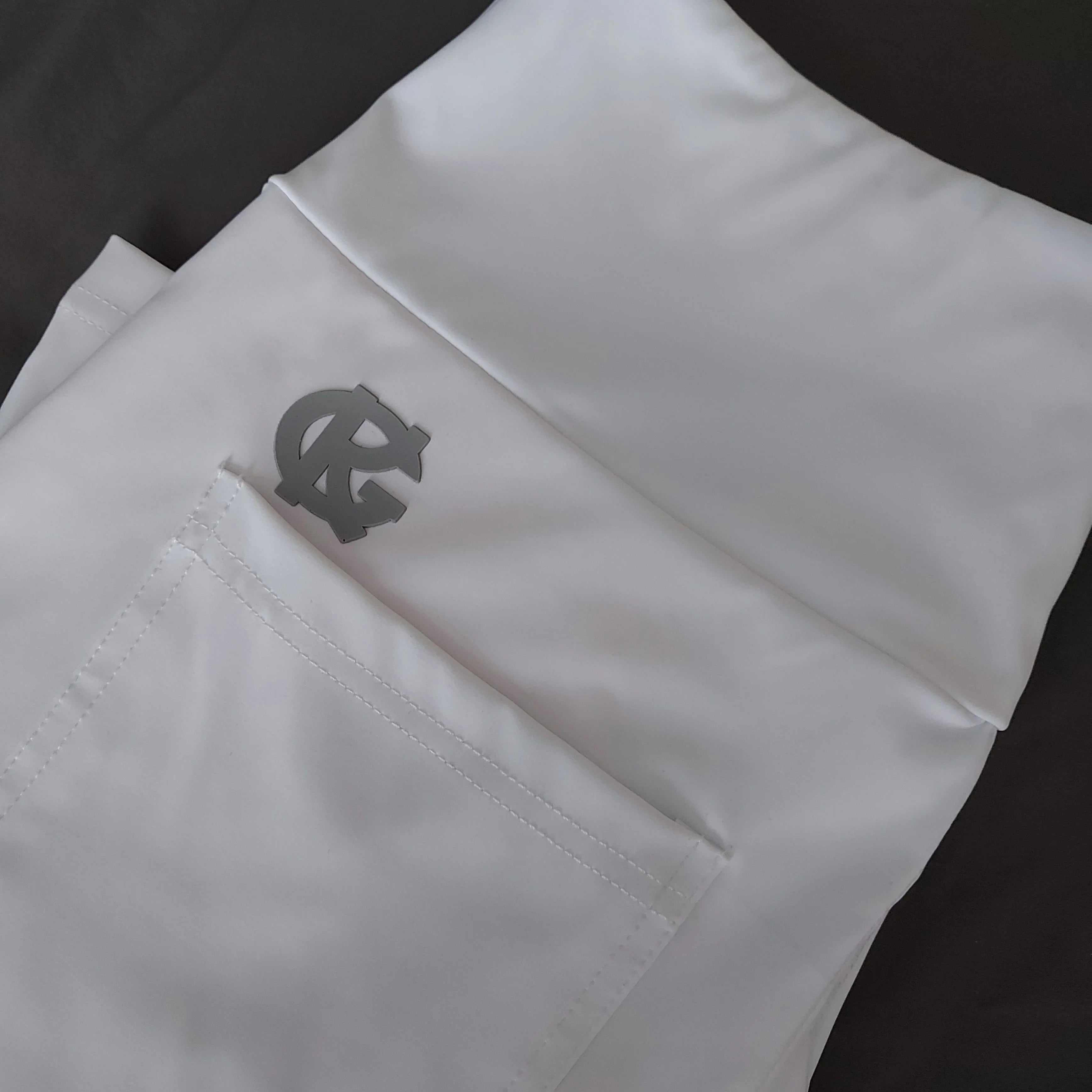 White scrub pants with gray RC logo on pocket, medical uniform on dark background