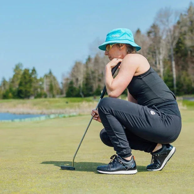 Woman golfer in turquoise hat and sunglasses lining up a putt on a sunny golf green