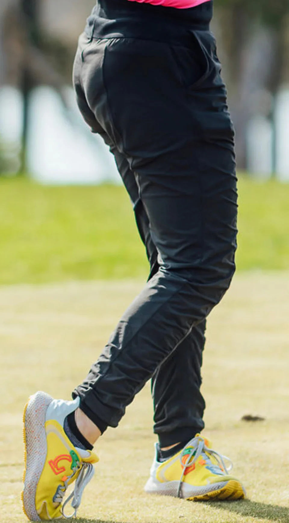 Person in black joggers and yellow athletic shoes walking on grass outdoors