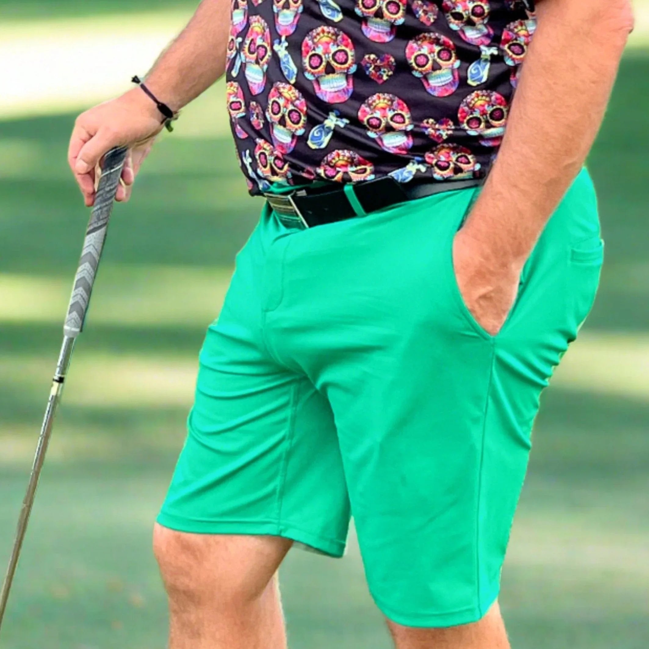 Man golfing in bright green shorts and a colorful skull print shirt on a grassy course