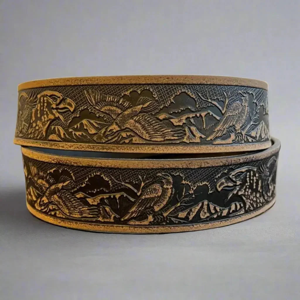 Men's grain leather belt with embossed eagle and mountain pattern, close-up view.