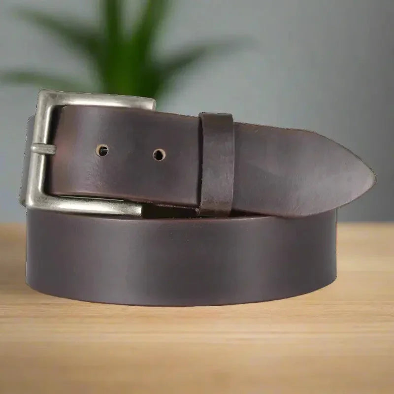 Men's solid brown leather belt with silver buckle on wooden table