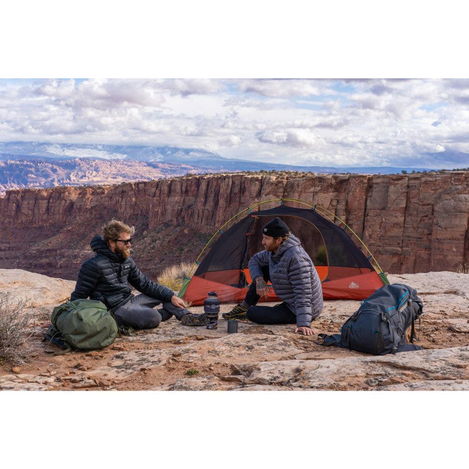 Two hikers camping near a cliff with Kelty Asher 55 backpacks, tent, and scenic canyon view