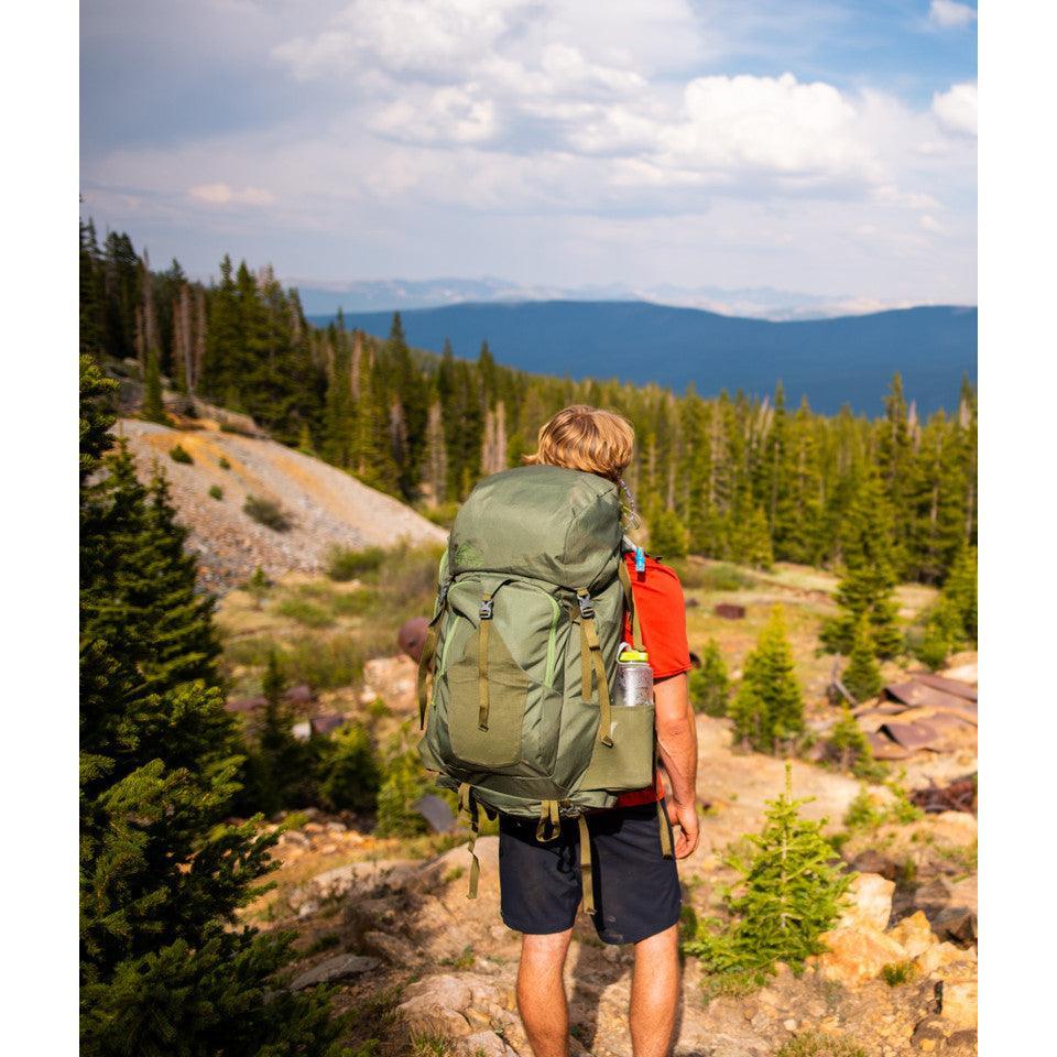 Hiker with Kelty Asher 85 backpack outdoors in a scenic mountain forest landscape