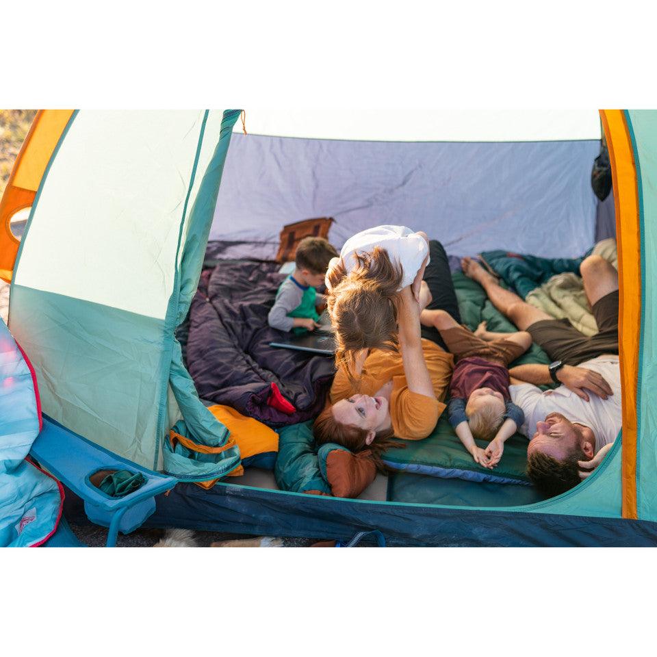 Family relaxing inside a camping tent with sleeping bags during outdoor adventure